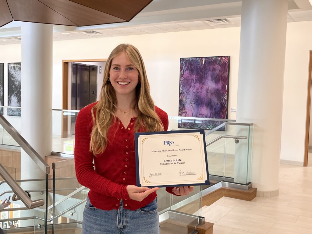 Emily Schulz posing for a photo holding her award certificate in the Schoenecker Center 2nd floor
