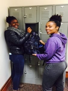 Library student workers Lorna Nakabuye and Sarah Kamba Binamu demonstrate the great feeling patrons get when their valuables are stored safely in a free locker at the library circulation desk.