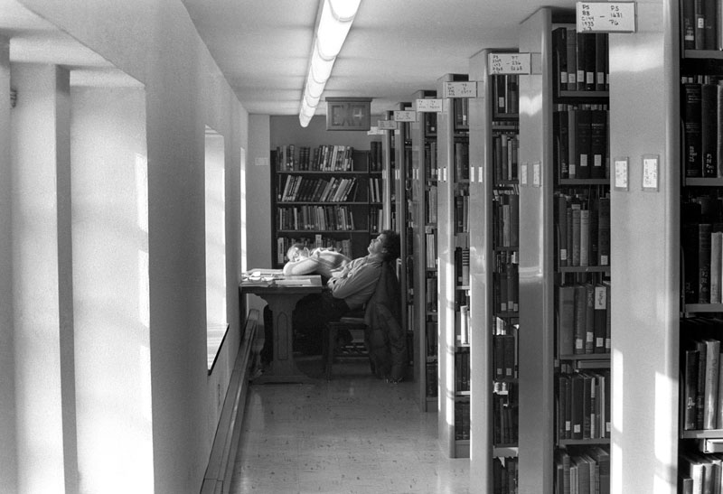 Black and white photo of two students sleeping by a window in the library stacks