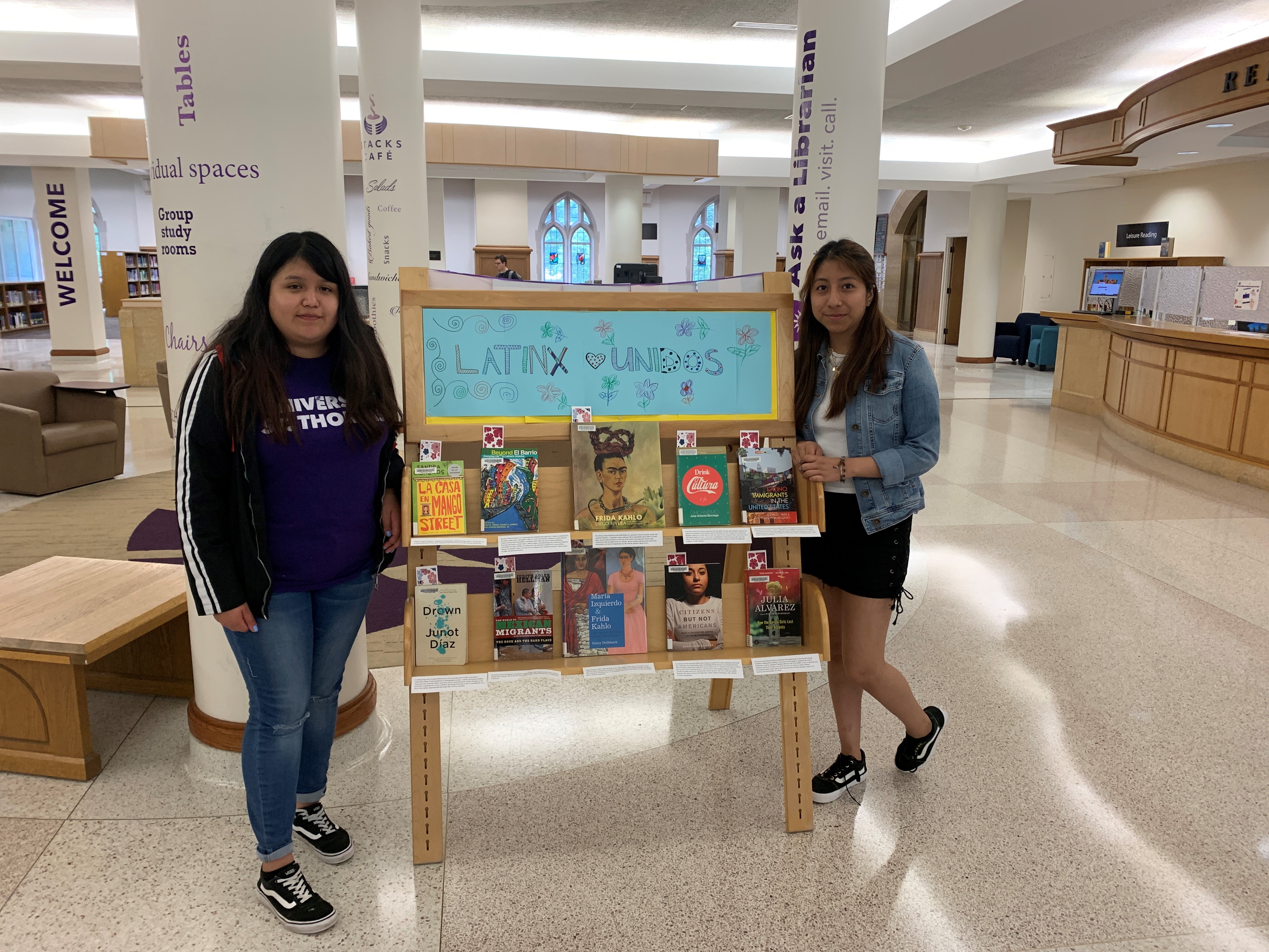 Two women stand in front of their book display titled "Latinx Unidos"