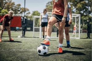 Woman standing with her foot on a soccer ball while other players stand ready behind her.