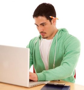 Young hispanic man in a light green jacket is typing on a laptop.